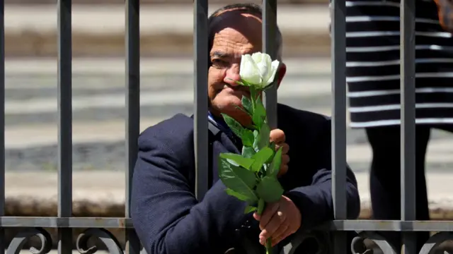 Antonio Siracusa com uma rosa branca apoiado nas grades de um portão