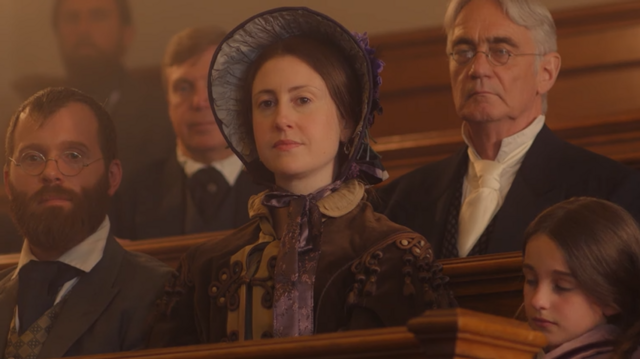 Mulher com trajes antigos sentadaapostar no bettribuna, rodeada por outras pessoas