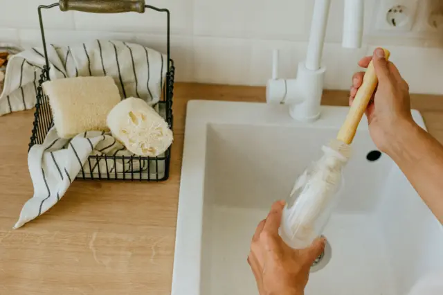 Seseorang mencuci botol kaca yang dapat digunakan kembali dengan sikat alami di dapur.