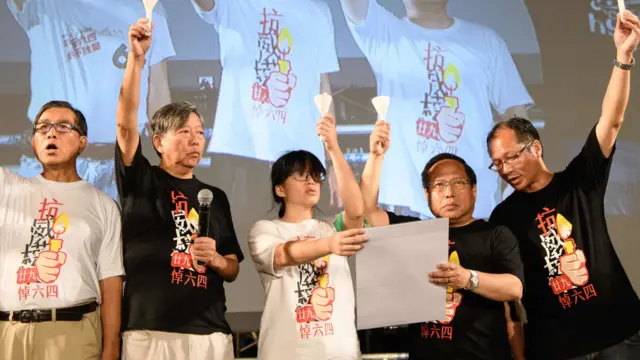 李卓人(左二)、鄒幸彤(中)、何俊仁(右二)在香港維多利亞公園「六四」燭光晚會主禮台上宣讀祭詞,各人伸出一隻手高舉白色蠟燭(4/6/2018)