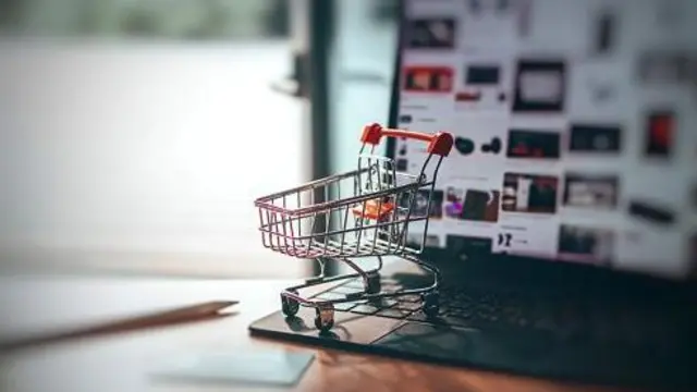 Колаж на тему інтернет-продажів, на клавіатурі ноутбука стоїть мініатюрна корзина на колесах, як у супермаркетах