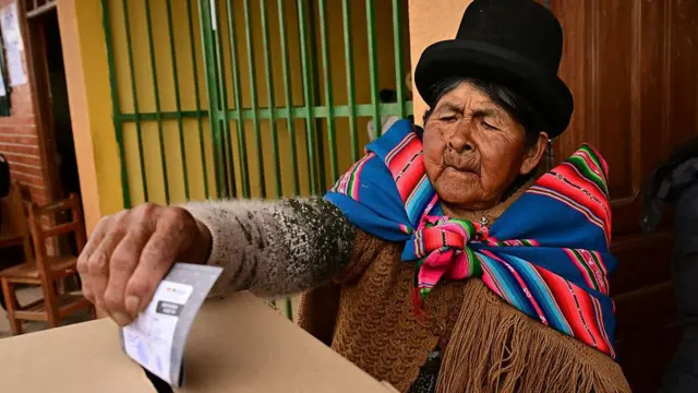 Una mujer con vestimentas indígenas deposita su voto en una urna