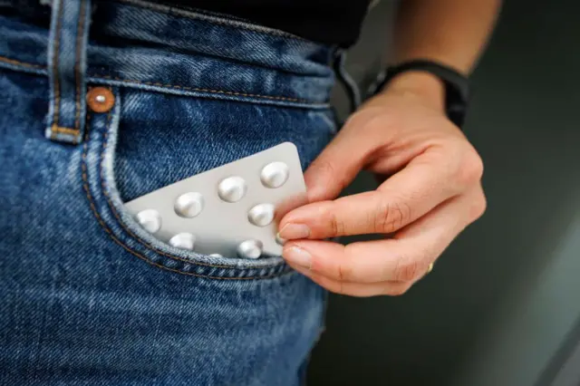 На цій фотографії людина витягує блістер таблеток з кишені.