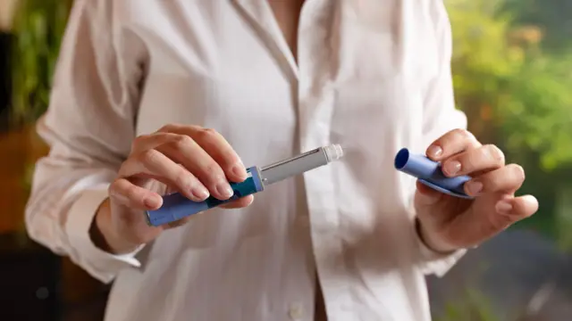 Zdjęcie stockowe przedstawia zbliżenie osoby trzymającej w dłoniach dwie części zastrzyku na odchudzanie. Zastrzyk wygląda jak długopis z zdjętą nasadką, a osoba ma na sobie różową bluzkę.