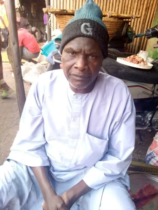 Malam Magaji Yusuf Zakari,habillé en blanc avec un bonnet sur la tête