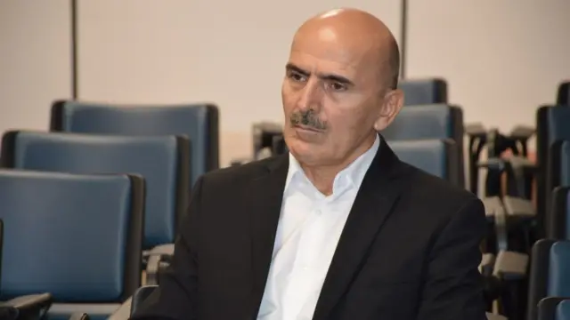 قاسم بیک محمد روی صندلی در سالنی نشسته است