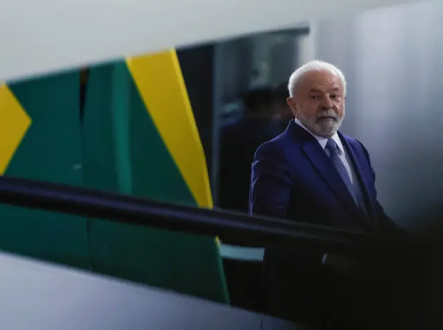 Lula caminhando,  com bandeira do Brasil ao fundo