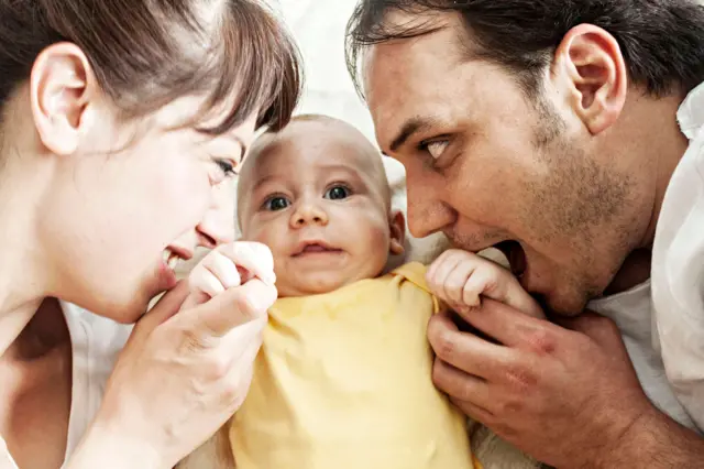 Young mother and father is biting and kissing their baby's hand, family having fun together
