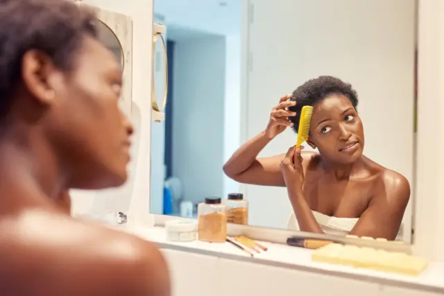 Femme qui se brosse les cheveux en se regardant dans le miroir