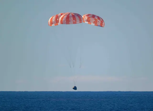 주황색 낙하산을 단 착륙 캡슐이 짙푸른 바다 위로 내려오고 있다
