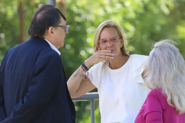 Mariana González, una mujer de pelo rubio, con anteojos y una camisa blanca, dialoga con una mujer y un hombre en las afueras de la prisión Rodeo I