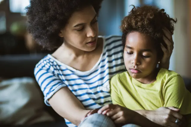 Mãe consola filho triste; eles estão abraçados e sentados 