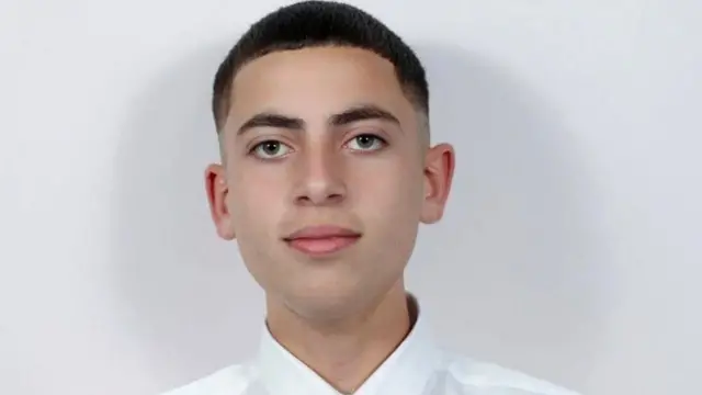 Tinejdžer sa kratkom tamnom kosom u beloj košulji. Gleda u kameru i blago se osmehuje. 