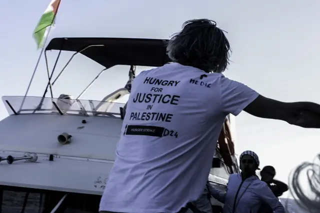 يظهر أحد أعضاء طاقم المتطوعين مرتدياً قميصاً أبيض كُتب عليه "متعطشون للعدالة في فلسطين" باللون الأسود، بينما تستعد سفينة الصمود العالمي للانطلاق من ساحل جزيرة كريت اليونانية في محطتها الأخيرة نحو غزة لكسر الحصار الإسرائيلي في كريت، اليونان، الصورة التقطت نهاراً.