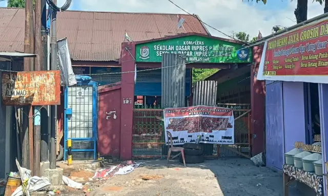 Sebuah spanduk melintang di pagar Kompleks SD Inpres Pajjaiang dan SD Inpres Sudiang. Tiga ban bekas, kursi, dan beberapa potong kayu disusun menutup gerbang.
