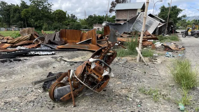 घाटी और पहाड़ की सड़क किनारे जले हुए स्कूटर और दुकानें