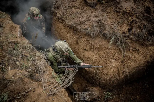 Двое военных с автоматами идут по окопу