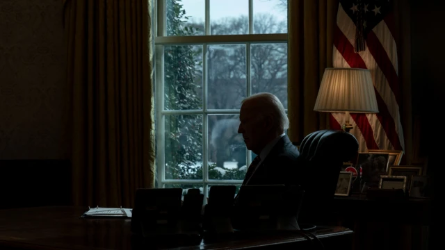 President Joe Biden receives a briefing at his desk in shadows