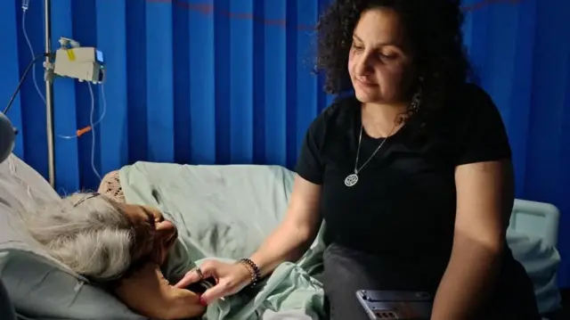 منى سيف، تجلس بجوار والدتها ليلى سويف، وهي نائمة على سرير وتتلقى العلاج بالمحاليل الطبية