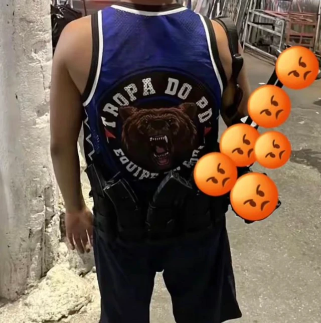 Jovem com fuzil nas costas e camiseta regata escrito Tropa do Urso