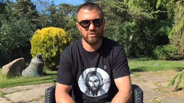 Ломаченко в футболці з Ісусом Христом сидить на вулиці поміж дерев