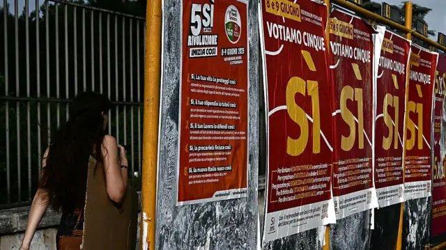 Женщина проходит мимо плакатов в поддержку референдума в центре Рима.