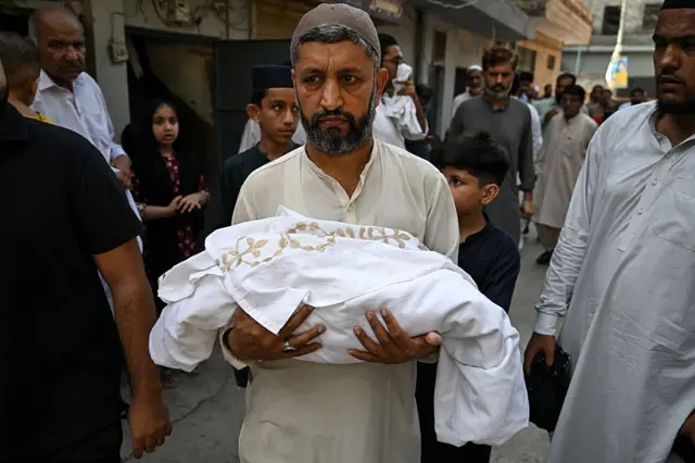 A man carries the body of a newborn child who died following a fire at the Mother and Child Health (MCH) ward of the Pakistan Institute of Medical Sciences (PIMS) Hospital, during a funeral in Rawalpindi on August 26, 2026. A fire erupted in a hospital maternity ward in Islamabad on August 26, killing 14 infants, Pakistan authorities said, blaming a faulty air conditioner for the blaze.