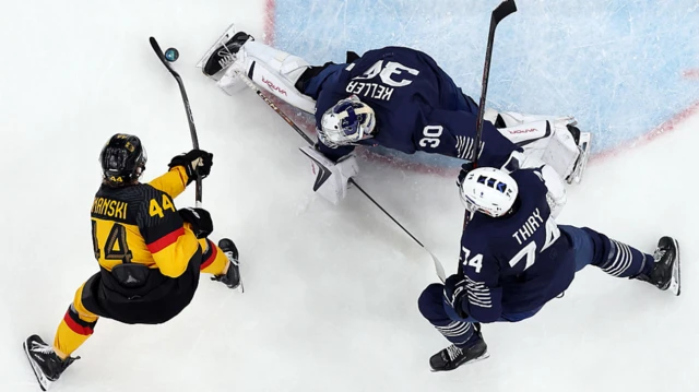 Хоккеист в желтой форме забрасывает шайбу вратарю в синей форме