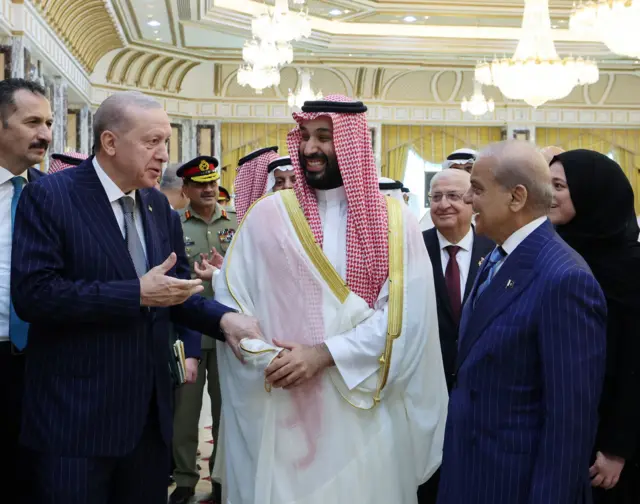 Erdogan, Bin Salman y Sharif sonríen mientras hablan entre ellos en un gran salón, donde caminan rodeados de gente.