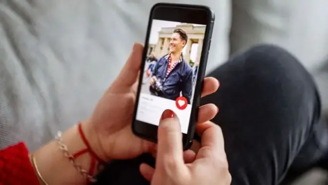 Mão segurando celular com aplicativo Tinder aberto