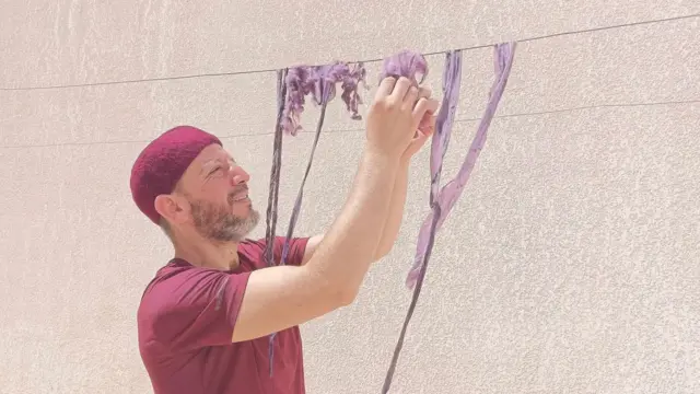 homem manuseando pano com tinta roxa