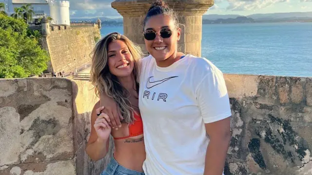 Aubrey, đứng bên trái, mặc bikini màu cam và quần short denim. Vợ cô mặc áo thun trắng của Nike. Cả hai đều mỉm cười nhìn vào máy ảnh, phía sau là khung cảnh biển.