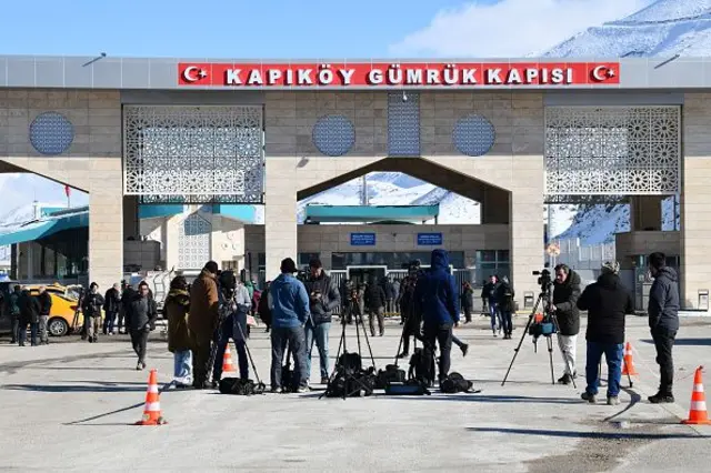 Van'daki Kapıköy sınır kapısı önünde gazeteciler kameralarını tripodlara yerleştirmiş arkaları dönük şekilde bekliyor. Geçiş yapan insanlar görünüyor. 1 Mart 2026. 