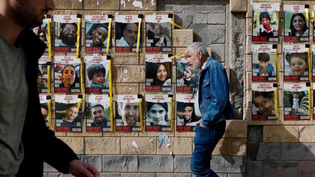 Israelis walk past banners bearing pictures of hostages kidnapped in a Hamas attack