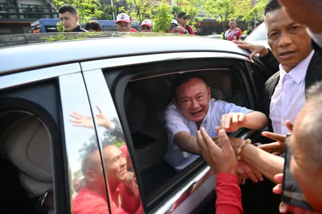ทักษิณลดกระจกรถยนต์ลงเพื่อให้ประชาชนได้เห็นและทักทายเขาในเวลาช่วงสุดท้ายก่อนออกจากประตูรั้วของเรือนจำกลางคลองเปรม