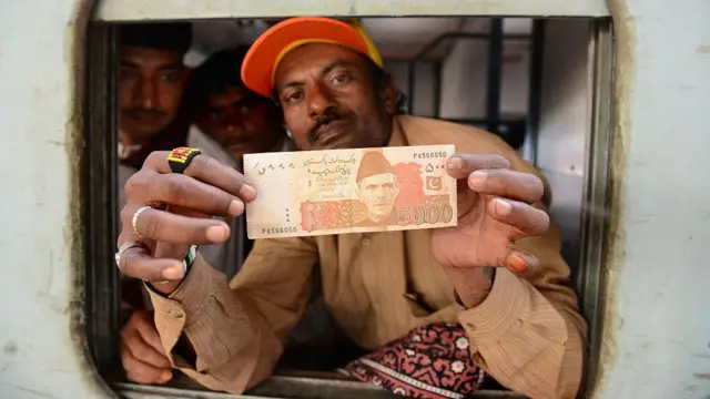 ایک شخص پانچ ہزار روپے کا نوٹ دکھا رہا ہے