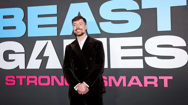 MrBeast na estreia do reality show 'Beast Games', cujo nome está escrito em branco sobre fundo preto atrás dele