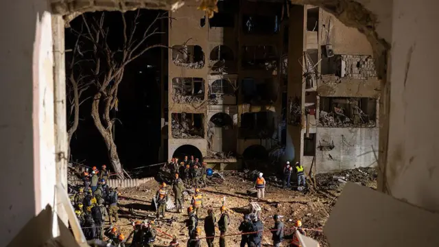 Аварийные службы собираются ранним утром 22 марта 2026 года на месте ракетного удара, нанесенного Ираном несколькими часами ранее в городе Арад (Израиль).