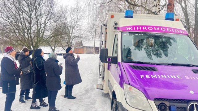 Cinq femmes vêtues d'épais manteaux et de bonnets se tiennent dans la neige devant la clinique mobile.