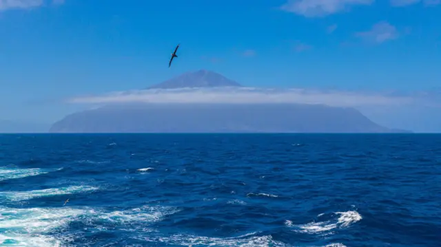 Vista de Tristão da Cunha com nuvens, o mar e uma gaivota voando