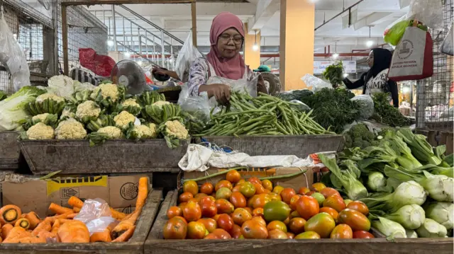 Pedagang sayur di Pasar Legi, Mistiyah, sedang melayani pembeli. Ia mengaku pasokan sayuran langka sejak ada makan bergizi gratis.