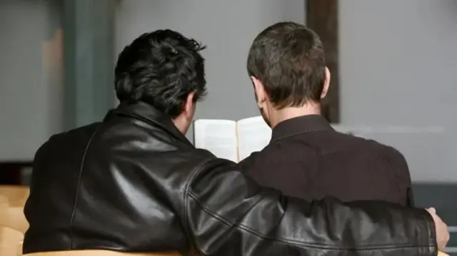 Una pareja de hombres abrazados leyendo la biblia