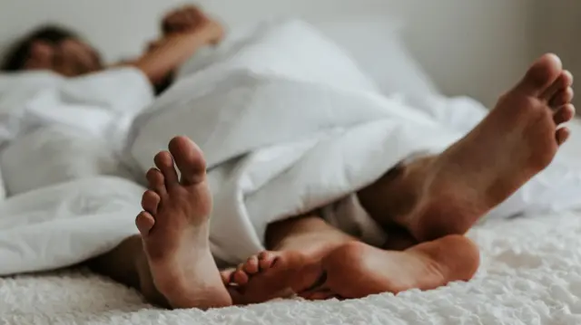 两双脚从床尾伸出来。背景中有一名男子,但画面呈现模糊状态