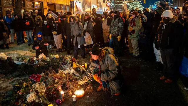 Personas colocando arreglos florales en el suelo, así como velas, para honrar la memoria de alex pretti. 