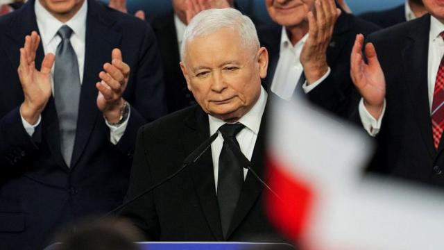  Jaroslaw Kaczynski fazendo discurso, rodeado por outras pessoas e bandeiras da Polônia