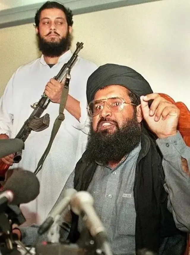 دوه سړي لیدل کېږي یوه سره ټوپک لاس کې دی بل وینا کوي.