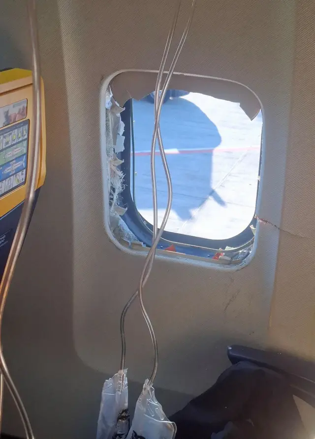 旅客機の窓が壊れている様子を機内から撮影した写真。酸素マスクが複数、降りている。窓の外には車両が停まっている地面が見える
