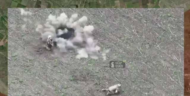 Зображення двох українських військових, які лежать на полі, а біля них відбуваються вибухи