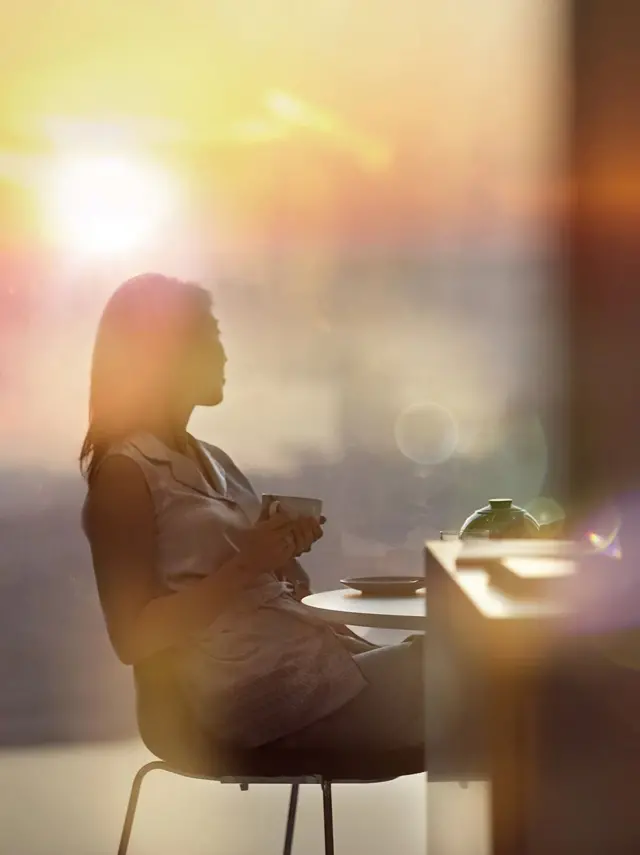 žena drži šoljicu kafe sa obe ruke i gleda levo od sebe