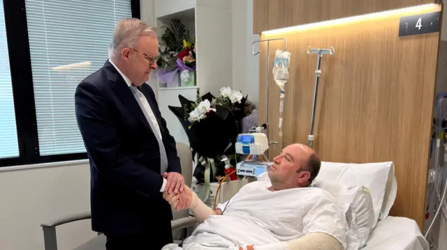 احمد الاحمد روی تخت شفاخانه خوابیده و در حال دست دادن با آنتونی آلبانیزی نخست وزیر استرالیا دیده می‌شود.